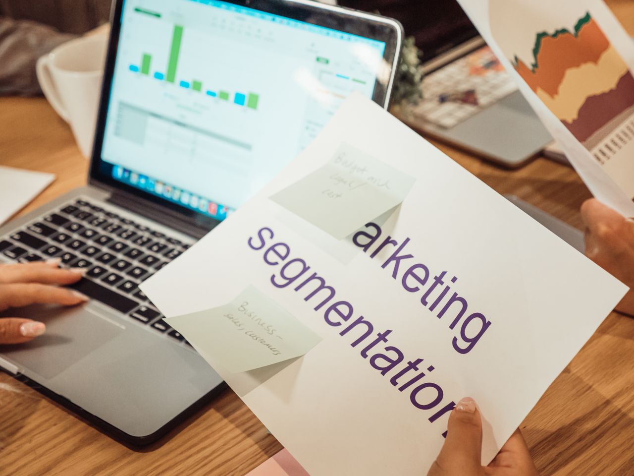 Un espace de travail moderne montrant des mains en train d’analyser des données marketing sur un ordinateur portable et des documents papier.